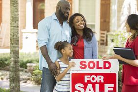 Parents and child standing by a âSoldâ sign with a real estate agent